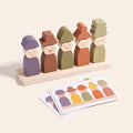 Five wooden peg dolls with different hats and faces on a plywood base, with pattern cards