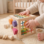 Baby pushing a wooden block through the elastic cords of the shape sorter cube