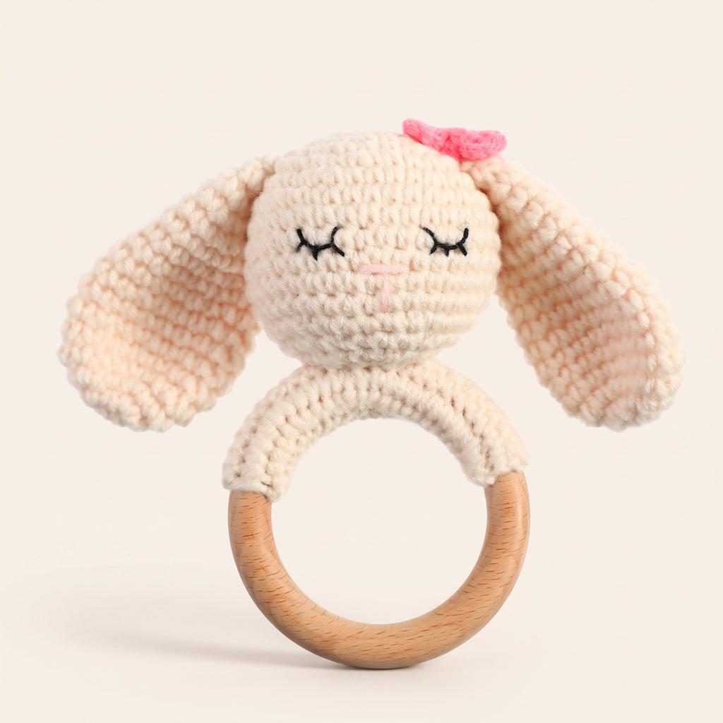 Cream crochet bunny rattle with floppy ears and a beech wood ring on a cream background