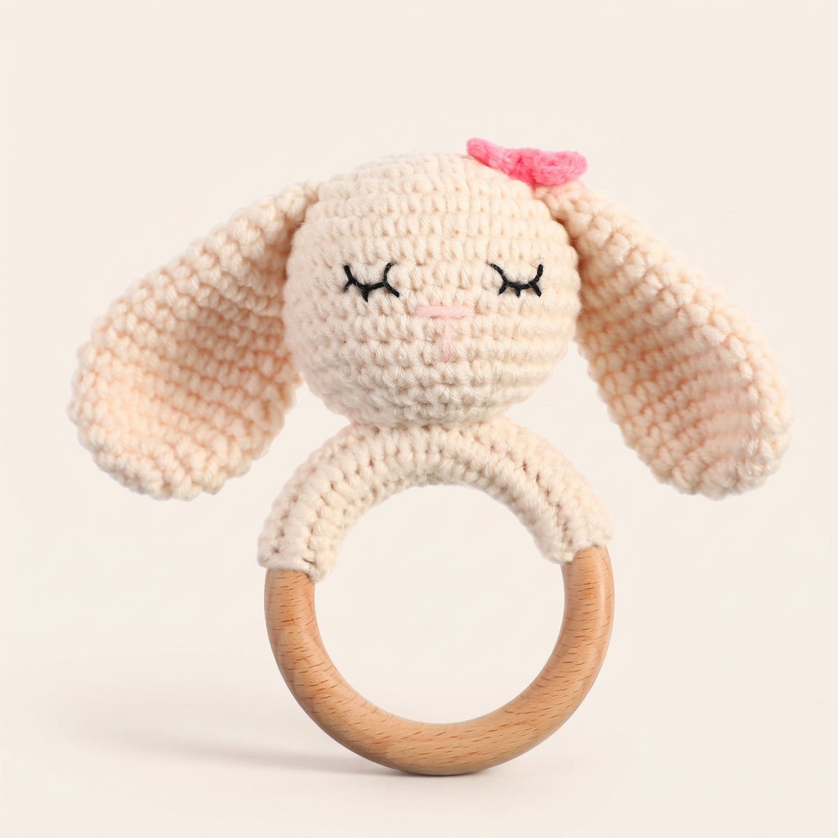 Cream crochet bunny rattle with floppy ears and a beech wood ring on a cream background