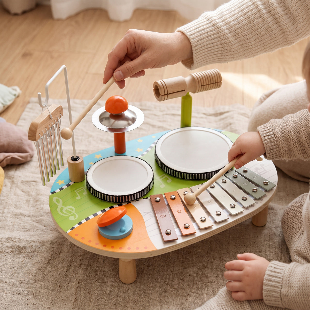 A parent ringing the wind chimes while a toddler plays the xylophone on the wooden music table