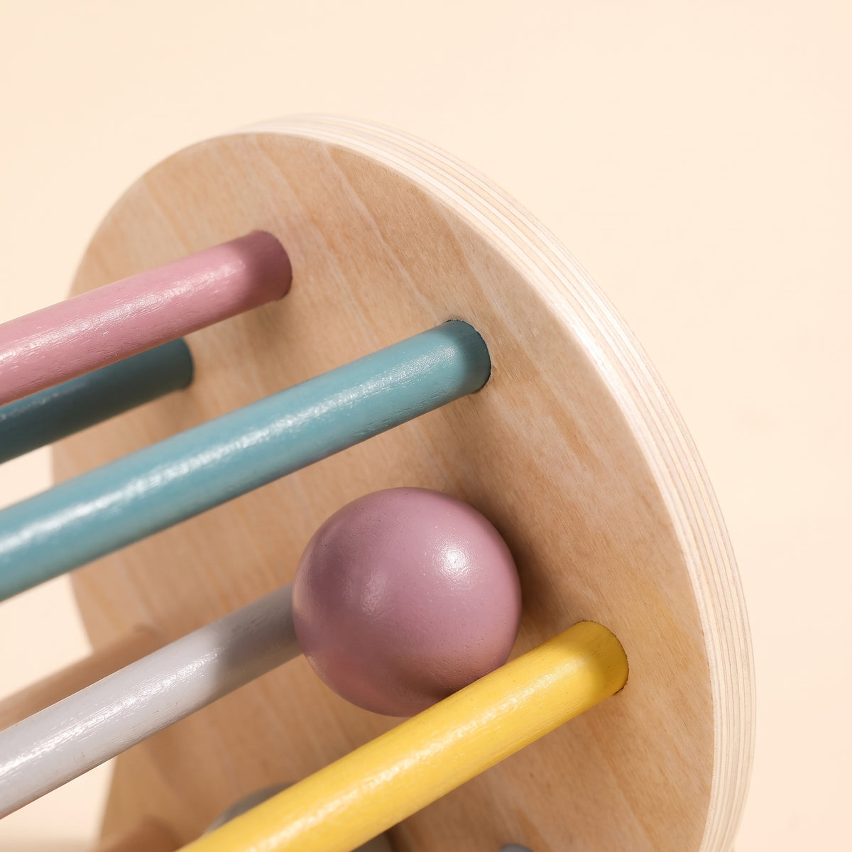 Close-up of the smooth plywood edge and pastel dowels of the wooden rolling drum toy