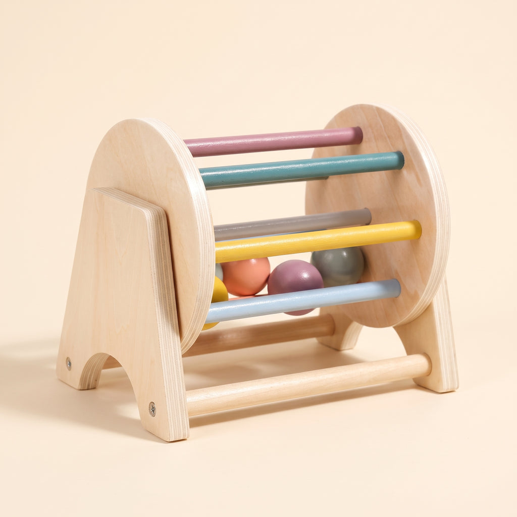 Wooden rolling drum toy with pastel dowels and wooden balls on a cream background