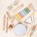 Pastel wooden musical instrument set laid out flat on a cream background: xylophone, tambourine, rain stick, maraca and more