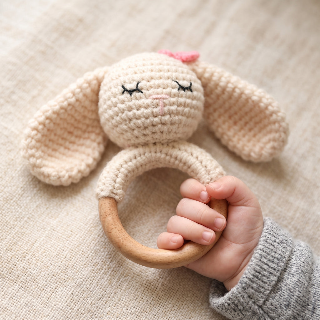 A baby's hand gripping the beech wood ring of the crochet bunny rattle