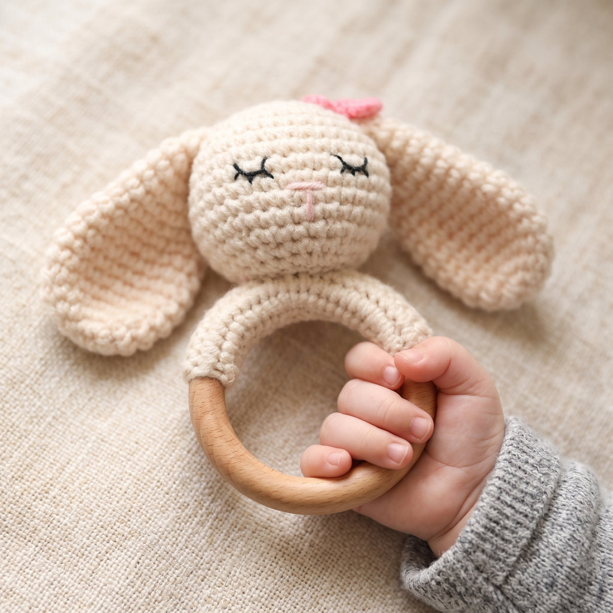 A baby's hand gripping the beech wood ring of the crochet bunny rattle