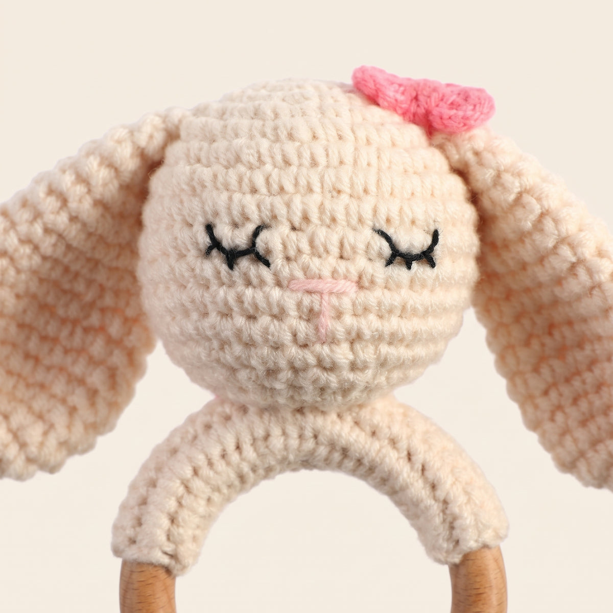 Close-up of the crochet stitches, embroidered sleepy eyes and pink bow of the bunny rattle
