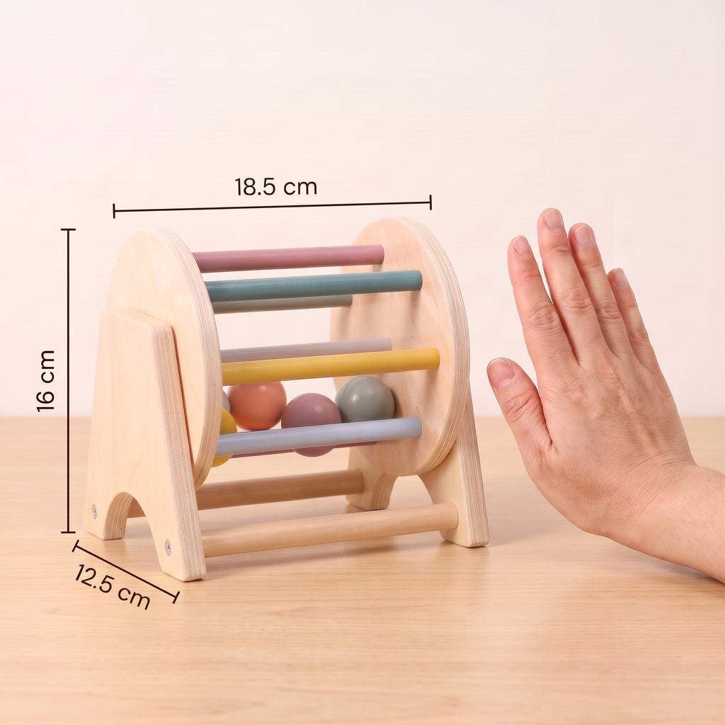 Wooden rolling drum toy next to an adult hand, measuring 18.5 cm wide, 16 cm high and 12.5 cm deep