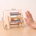 Wooden rolling drum toy next to an adult hand, measuring 18.5 cm wide, 16 cm high and 12.5 cm deep